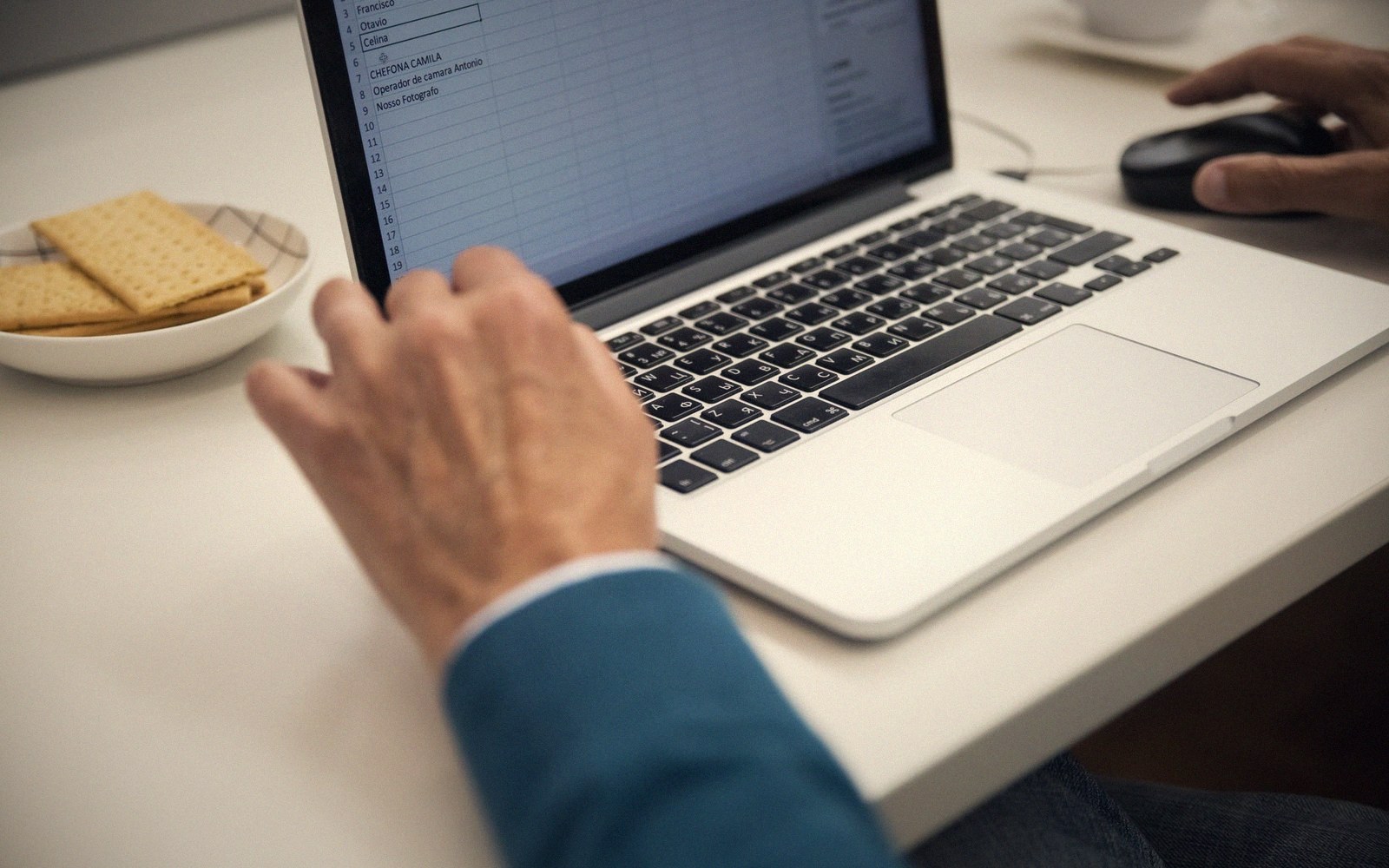 Hands typing on a laptop keyboard beside a plate of crackers on a desk